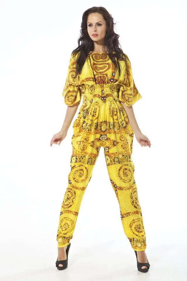 Model wearing a silk kimono-sleeve jumpsuit with gold-toned Klimt-inspired print, shirred from under-bust to waist.